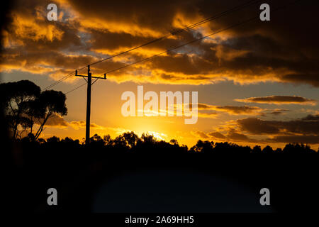 Golden sunsetting over natural landscape with electricity pylon running above. Stock Photo