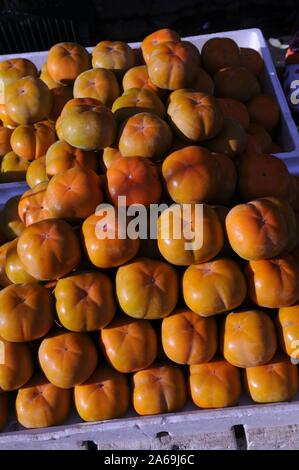 Sunlit stacked persimmons on display & for sale at an open air fresh fruit stall, The Russian Market, Phnom Penh, Cambodia. © Kraig Lieb Stock Photo