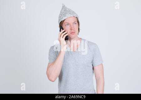 Young man with tin foil hat thinking while talking on the phone