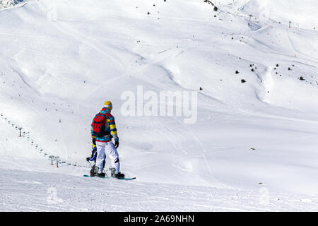 PYRENEES, ANDORRA - FEBRUARY 13, 2019: A snowboarder in bright clothes stands on a mountainside and prepares for the descent. Mountainsides and a lift Stock Photo