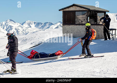 PYRENEES, ANDORRA - FEBRUARY 13, 2019: Rescuers at a ski resort provide assistance to the victim to evacuate him to the doctor. Two rescue workers lay Stock Photo