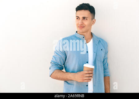 Outdoors Leisure. Stylish guy standing isolated on white with cup of coffee looking aside smiling curious Stock Photo