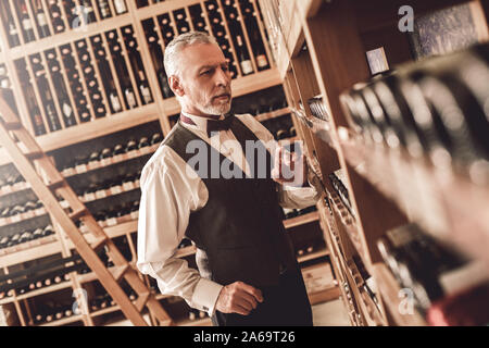 Sommelier Concept. Senior man standing choosing wine concerned Stock Photo
