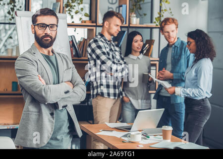 Startupers working together at office bearded man in glasses close-up looking camera confident while colleagues discussing documents Stock Photo