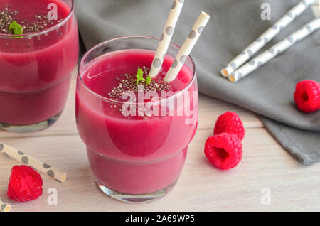 Red fruit raspberry smoothie in glass topped with chia seeds and mint on wooden table. Raw diet detox drink for health life. Stock Photo