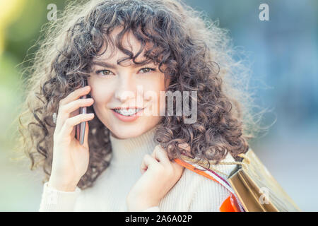 Portrait of a happy modern girl with dental braces and and curly hair.  Happy woman with shopping bags and smarphone. Stock Photo