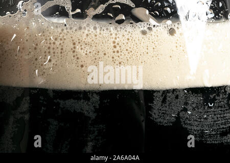 Macro shot glass of Beer with foam bubbles texture background. Craft dark beer flowing foam with sparkling bubbles. Beer foam texture close up. Stock Photo