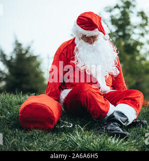 Stock photo of Santa claus sitting on the lawn, with his red sac. Christmas time and Noel Stock Photo