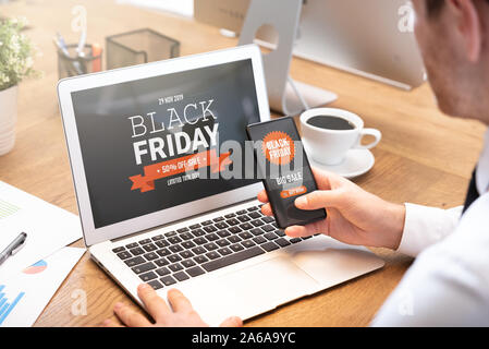 Black Friday promotion sale on laptop and phone screen. Young man doing shopping online Stock Photo
