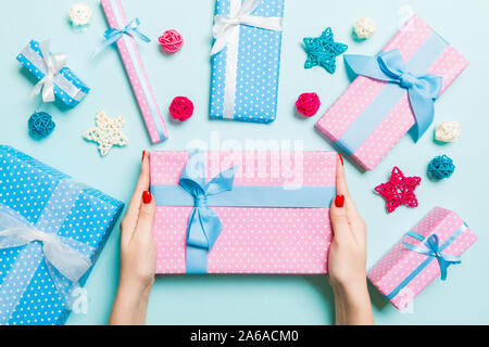 Top view of female hands holding a Christmas present on festive blue background. Holiday decorations. New Year holiday concept. Stock Photo