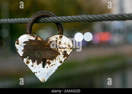 Heart shaped heavy rusty antique lock on urban street background. Vintage padlock on rope. Romantic love concept, fading away feelings of love. Stock Photo