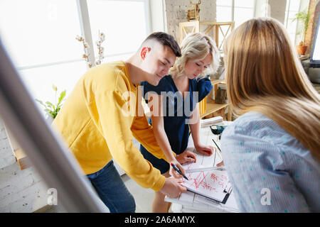 Interior designer working with young couple. Lovely family and professional designer or architector discussing conept of future interior, working with colour palette, room drawings in modern office. Stock Photo