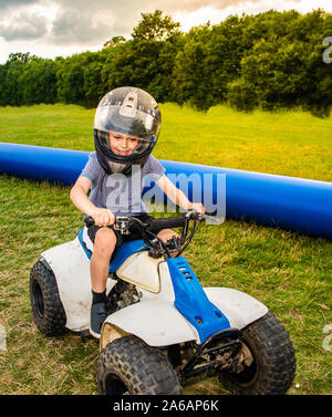 Little boy with ADHD, Autism, Aspergers Syndrome riding a quad bike smiling, laughing and having fun, crash helmet and visor on
