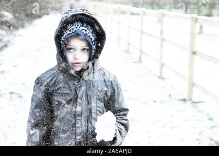 A little boy with ADHD, Autism, Aspergers Syndrome playing in the heavy snow fall, making snow balls, snowing at Christmas, Xmas, Christmas Eve Stock Photo