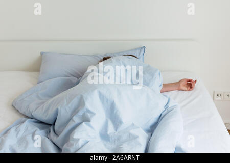Part of the home or hotel interior, woman sleeping on a white bed with blue linens in the morning in the sun Stock Photo