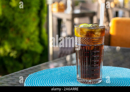 Alcohol cocktail - Long Island Iced Tea. Iced tea with lemon in a glass. Brown ice drink on table an outdoor in a cafe. Stock Photo