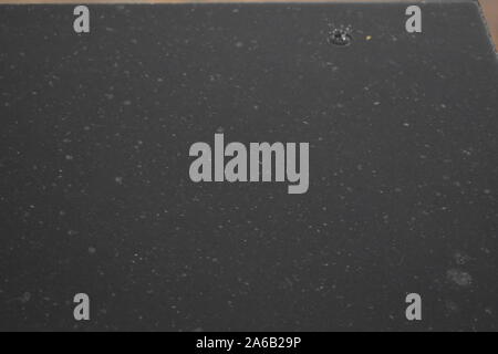 rain drops on the surface of water in a granite stone with graduated shade of black shadow and reflection of blue sky Stock Photo