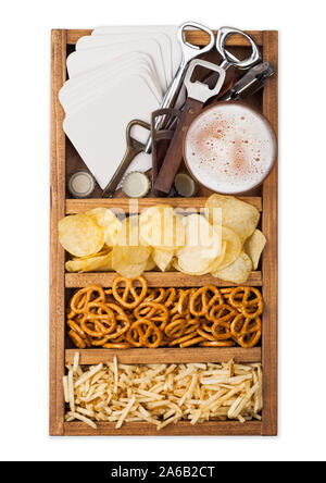 Glass of craft lager beer in vintage box of snacks openers and beer mats isolated on white. Pretzel and crisps and salty potato. Stock Photo