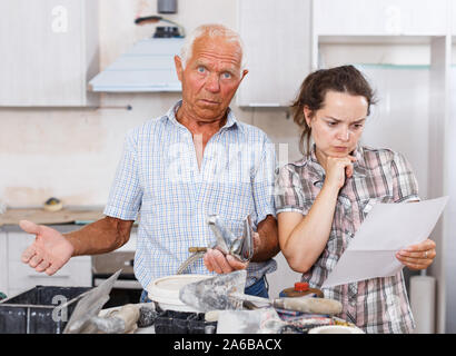 Perplexed young woman and senior man standing with mixer tap and paper in hands in their repairable house Stock Photo