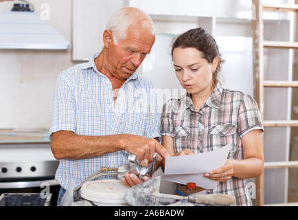 Young woman and her elderly father discussing instructions for installing mixer tap during repairs in their apartment Stock Photo