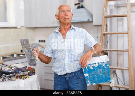 Senior man working on his house overhaul, determining scope of plastering works indoors Stock Photo