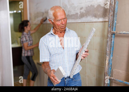 Skillful older man engaged in renovation work indoors with female assistant Stock Photo