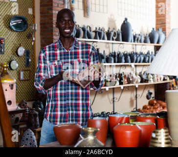 Friendly young salesman of pottery store offering traditional African handmade ceramic goods Stock Photo