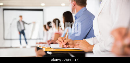 Woman making notes during lecture, focus on female hand with pen Stock Photo