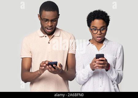 Head shot shocked African American couple using phones, reading news Stock Photo