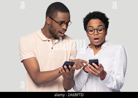 Head shot surprised African American couple sharing news, using phones Stock Photo