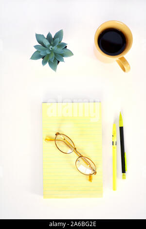 Coffee in yellow mug and notepad with pen and pencil and eyeglasses. In flat lay composition.  Vertical format. Stock Photo