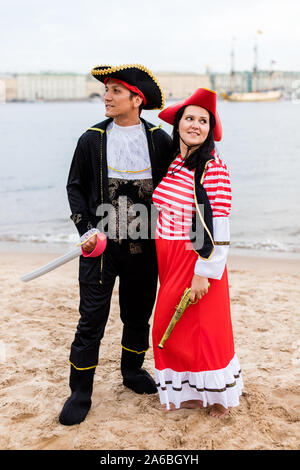 Young Caucasian man and woman in pirate costumes stand next to each other and look in different directions on sandy beach. Vertical. Stock Photo