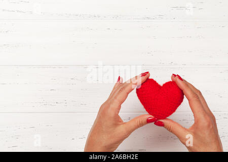Woman hands holding Valentine's red heart toy over wooden background. Top view with copy space Stock Photo