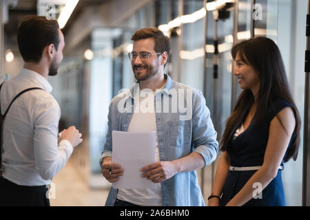 Smiling diverse colleagues talking, standing in office hallway Stock Photo