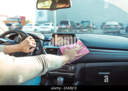 Close-up, hand wipes car interior from dust, car cleaning and tidying, in summer in parking lot near shopping center. Touch screen, steering wheel and Stock Photo
