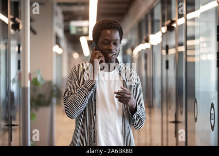 Smiling African American man talking on phone in office hallway Stock Photo