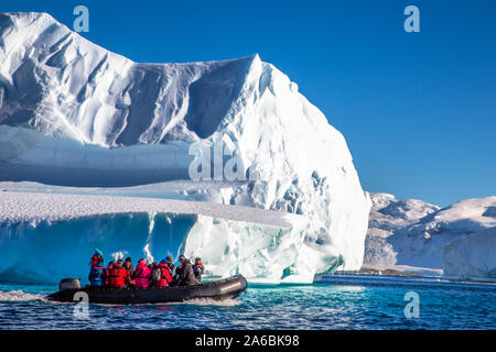 Tourists sitting on zodiac boat, exploring huge icebergs drifting in the bay near Cuverville island, Antarctic peninsula Stock Photo