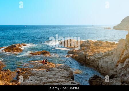 Sea. Young couple on a rocky coast at sunset.  Romantic summer landscape. Stock Photo