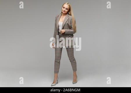 Smiling young elegant businesswoman with bright makeup and in suit looking down in the studio, isolated on grey background. Model girl in the business Stock Photo