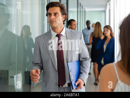 Portrait of focused successful businessman walking along busy office corridor Stock Photo