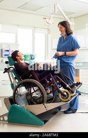 A dental nurse speaks to a disabled patient in a specialist wheelchair friendly dental chair Stock Photo