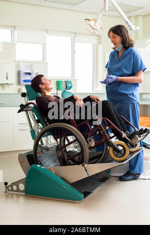 A dental nurse speaks to a disabled patient in a specialist wheelchair friendly dental chair Stock Photo