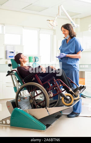 A dental nurse speaks to a disabled patient in a specialist wheelchair friendly dental chair Stock Photo