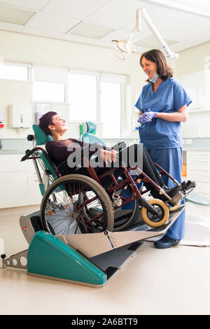 A dental nurse speaks to a disabled patient in a specialist wheelchair friendly dental chair Stock Photo