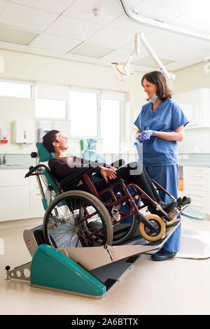 A dental nurse speaks to a disabled patient in a specialist wheelchair friendly dental chair Stock Photo