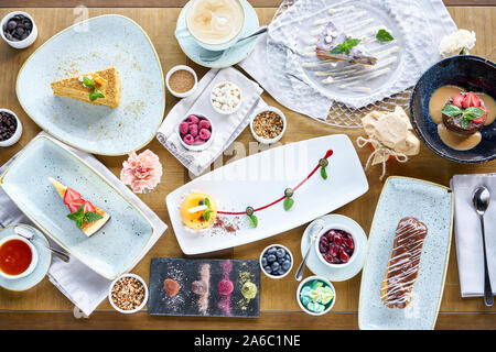 Breakfast in the cafe, morning coffee. Cappuccino and lots of desserts on the table. Eclair, mousse cake, chocolate truffle and cheesecake, Stock Photo