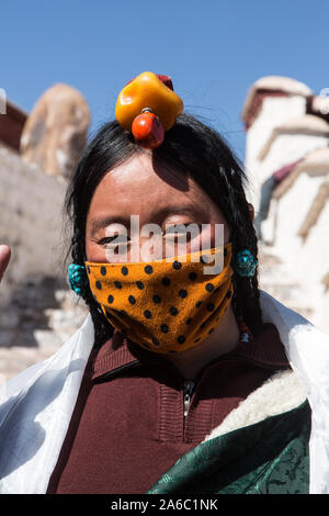 A Khamba Tibetan woman from the Kham region of eastern Tibet with her hair in traditional style with a headdress of red coral.  She wears a mask. Stock Photo