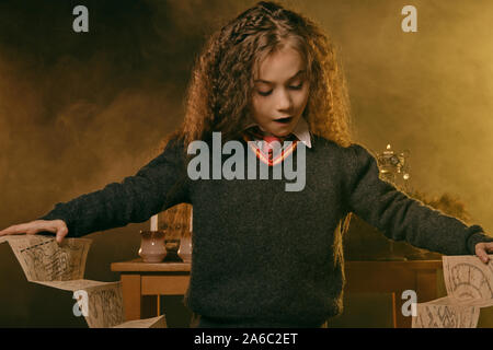 Portrait of a charming little charmer with magnificent long brown hair dressed in a navy blue jumper, white shirt and red tie. She is standing near a Stock Photo