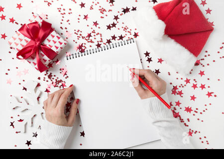 Wish list for Christmas and New Year. New 2020 year plan and red Holiday decorations, ruled notebook and female hands with wish list on white table. V Stock Photo