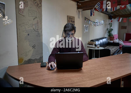Young man with beard working with his lap top in a desk of a hostel Stock Photo